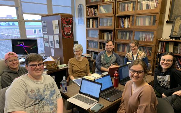 Candid image of Dr. Karen Winstead and student consultants sitting around a table with laptops, pausing for a moment to smile while working on an open-source English textbook